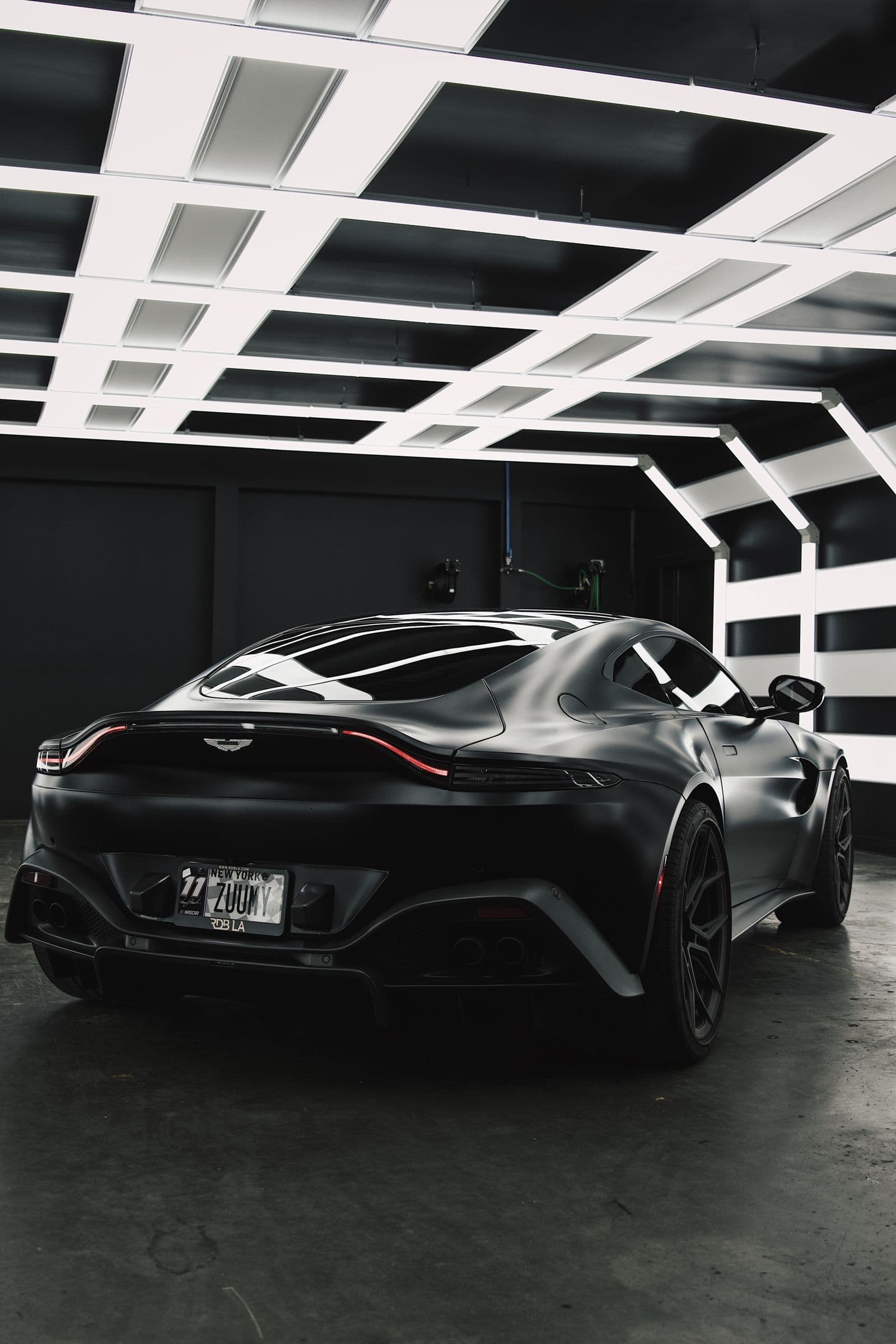 Black grand tourer under a geometric ceiling in a dark gloss-floored private garage — a design example